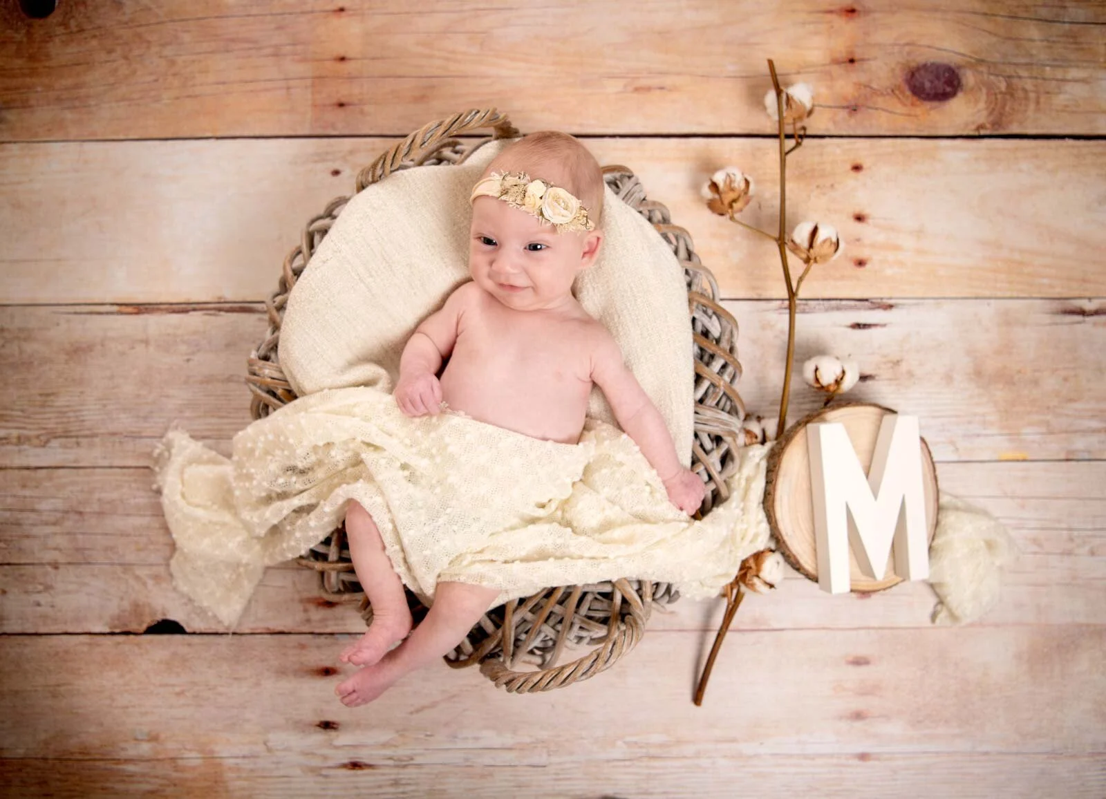Mit Holzbuchstabe | Peter Lauritis Photography Baby mit Haarband im Korb auf Holzboden, daneben Baumwollzweig und Holzbuchstabe