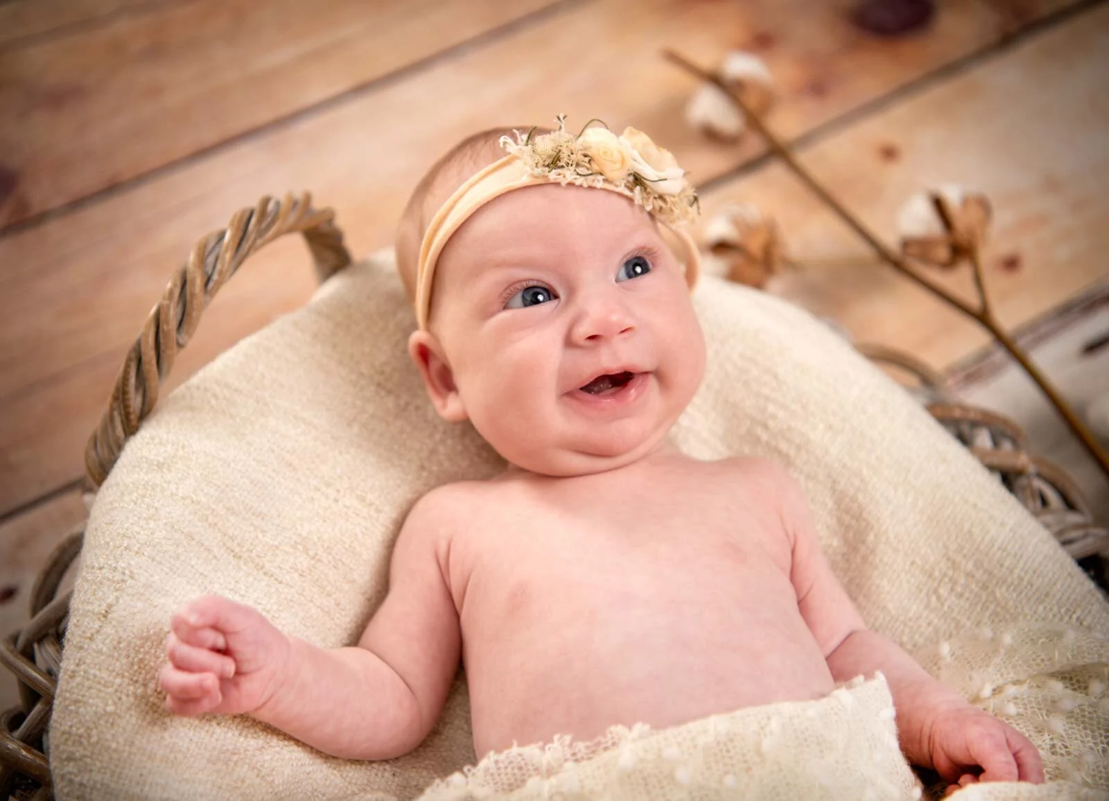 Lächeln mit Haarband | Peter Lauritis Photography Babyfotoshooting: lächelndes Baby mit Blütenhaarband liegt im Weidenkorb