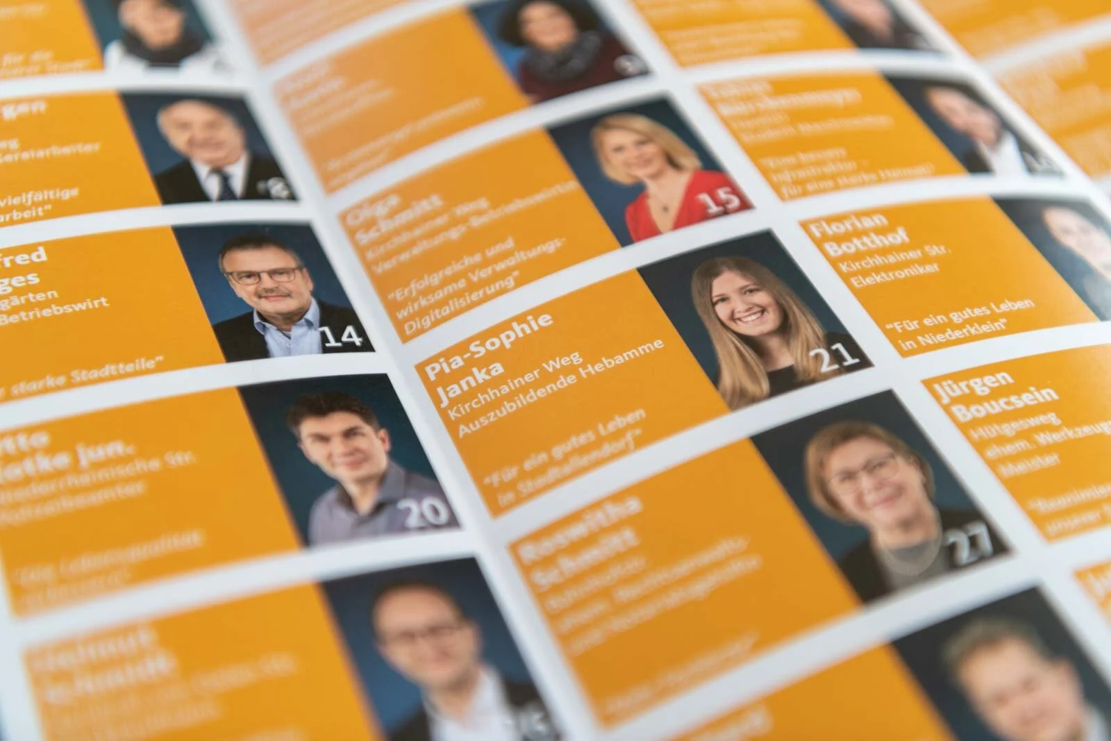 Nahaufnahme vieler Kandidatenportraits auf orangefarbenem Grund im Wahlflyer