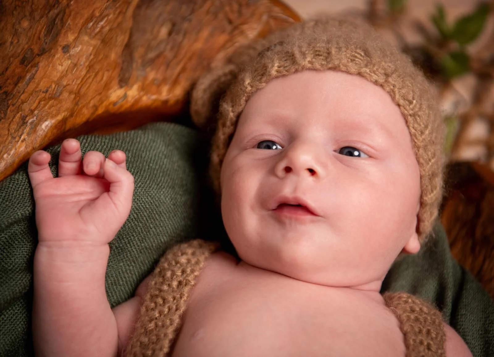 Baby mit brauner Strickmütze schaut mit großen Augen, ein Händchen erhoben