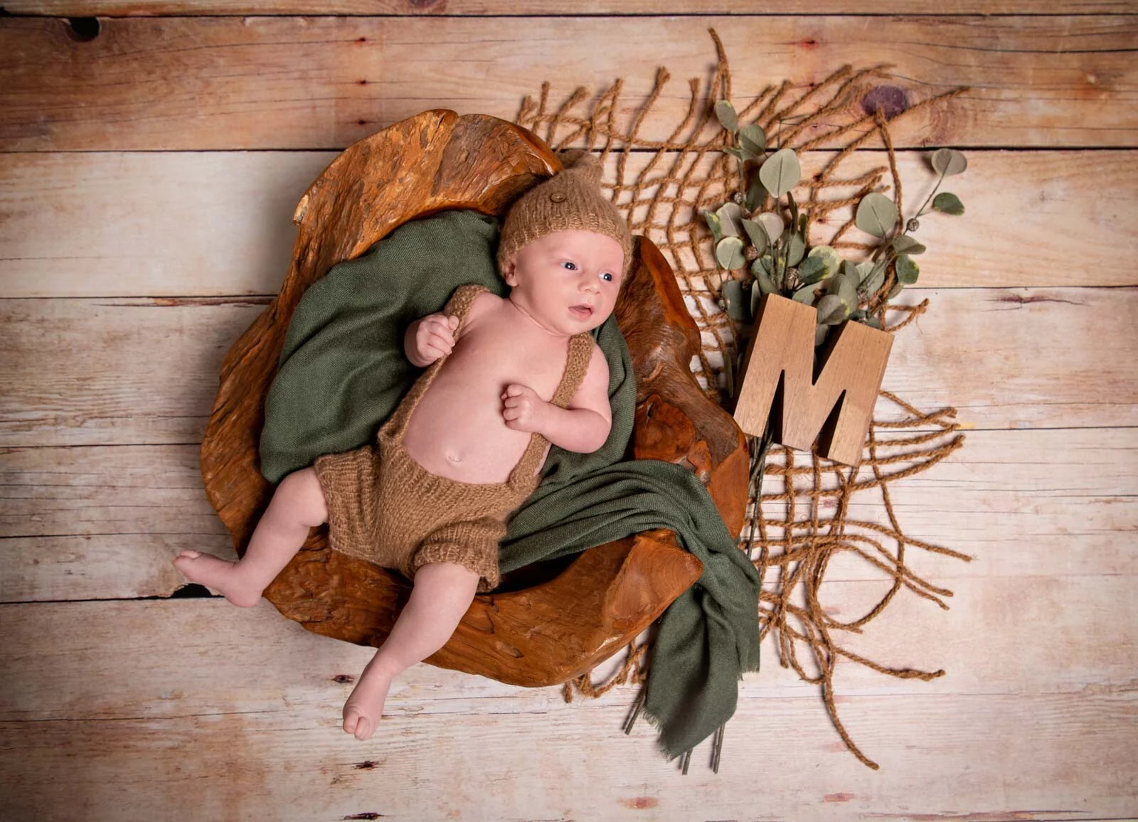 Babyfotos von oben: Neugeborenes in Holzschale auf Jute neben Holzbuchstabe und Eukalyptus
