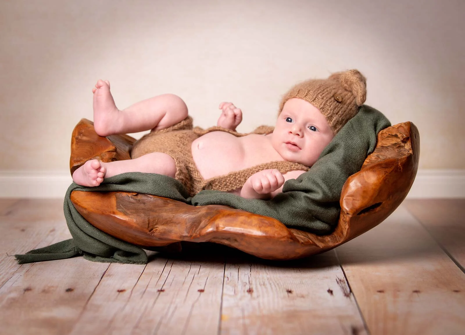 Babyfotos im Studio: Neugeborenes mit Strickmütze liegt in einer Holzschale