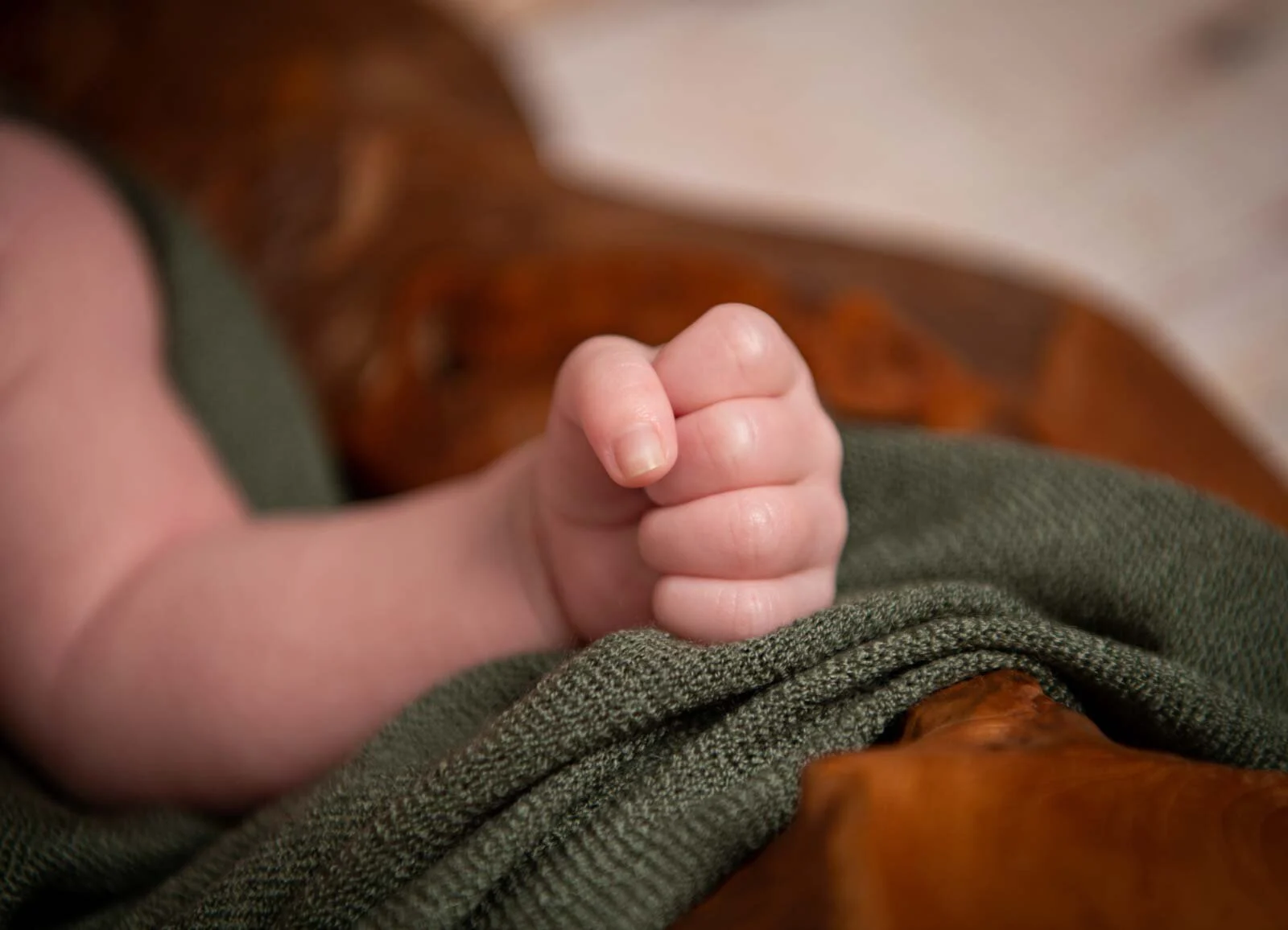 Nahaufnahme einer kleinen Babyfaust auf einer grünen Strickdecke in einer Holzschale
