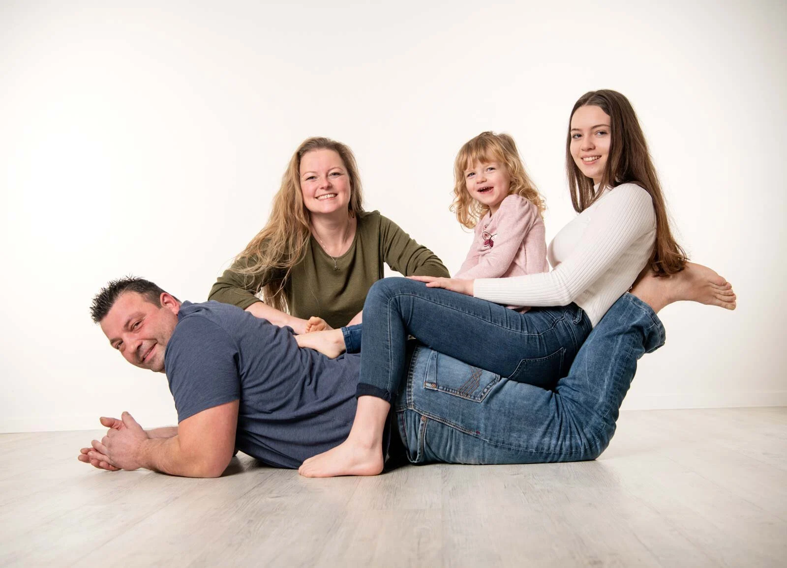 Familie mit zwei Töchtern liegt und sitzt lachend auf dem hellen Boden im Fotostudio