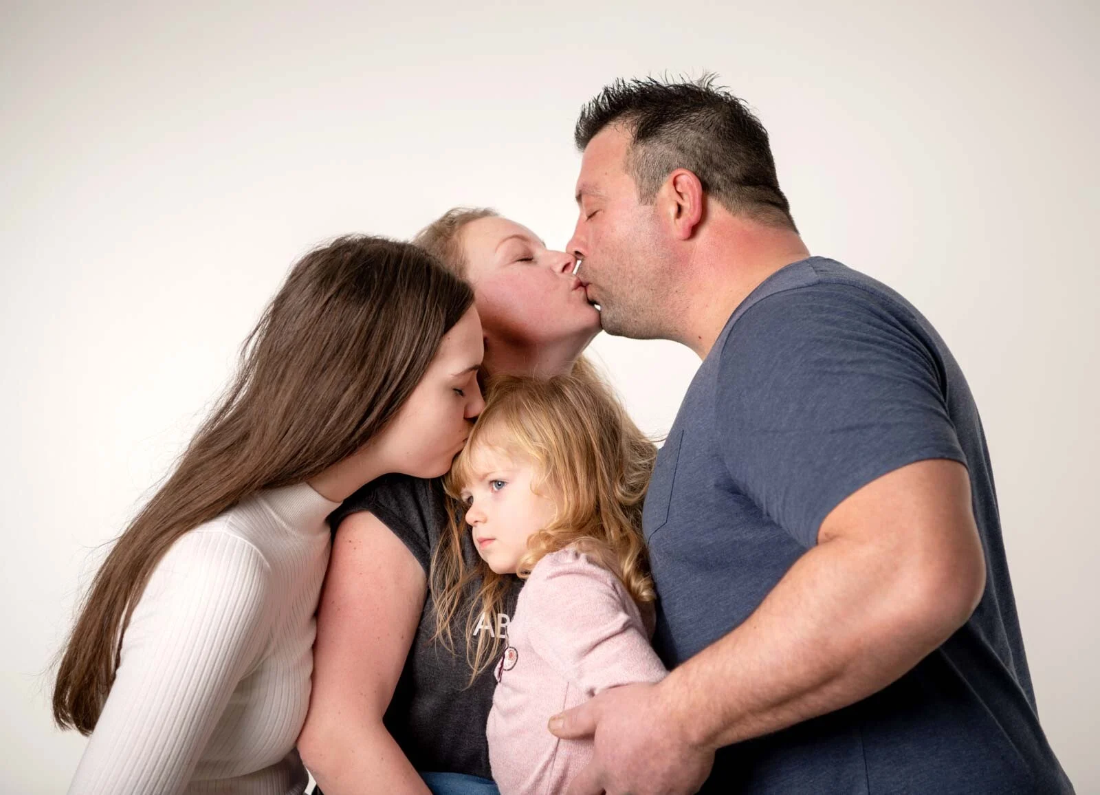 Gutschein für ein Fotoshooting: Eltern küssen sich, die Töchter kuscheln sich an