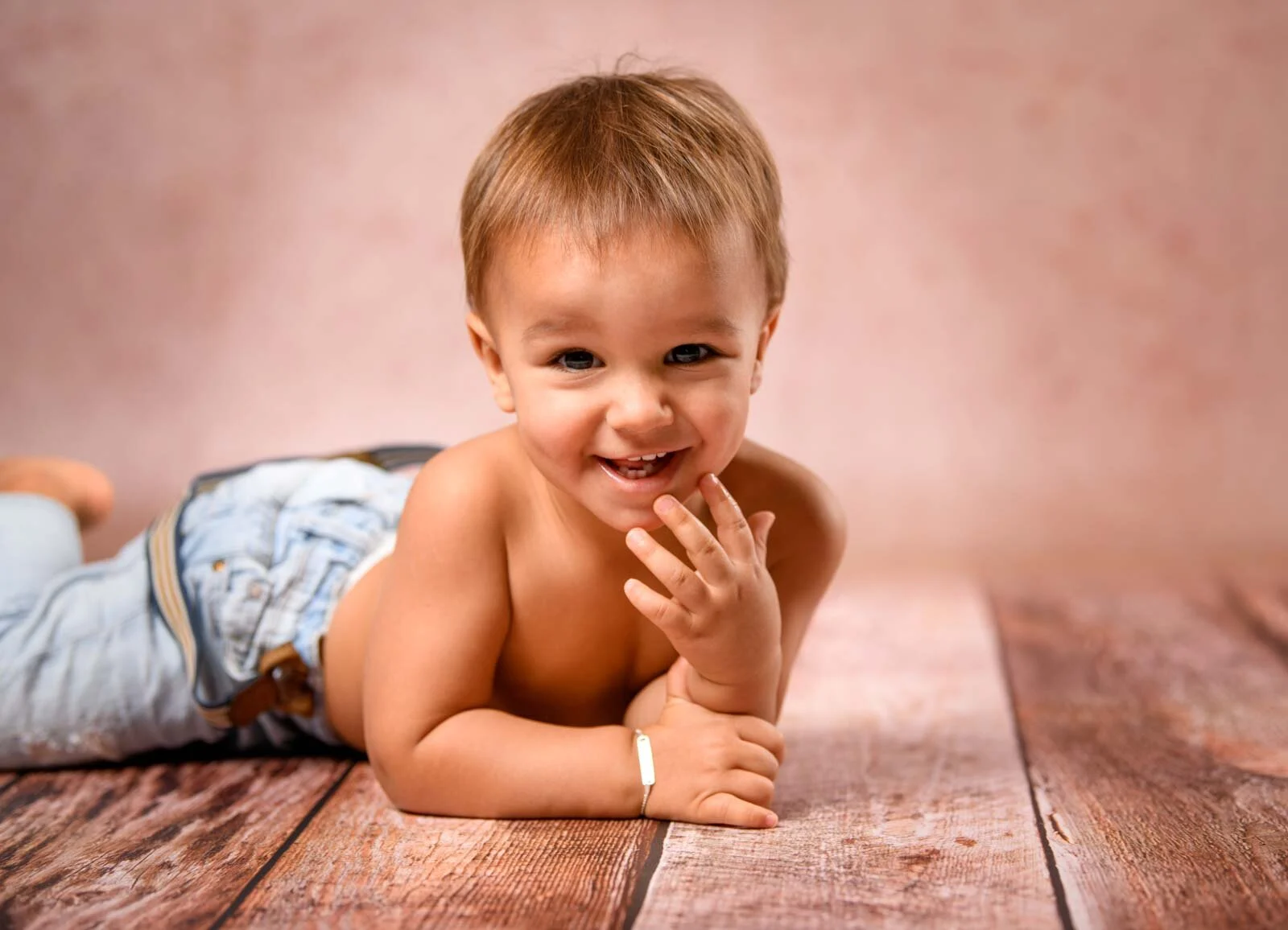 Kleiner Junge liegt lachend auf dem Bauch auf einem Holzboden im Fotostudio
