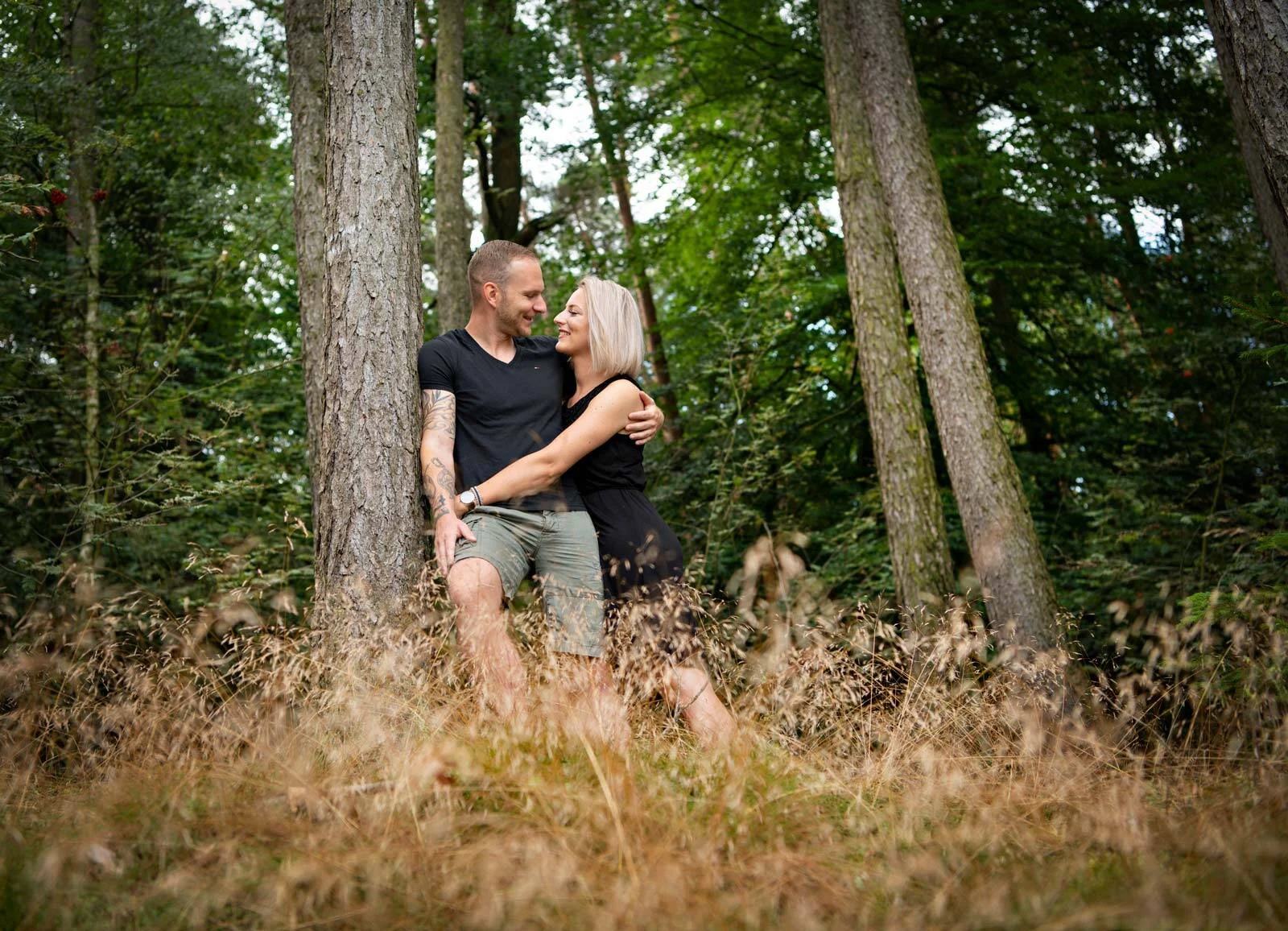 Paar steht eng umschlungen zwischen hohen Kiefern im Wald