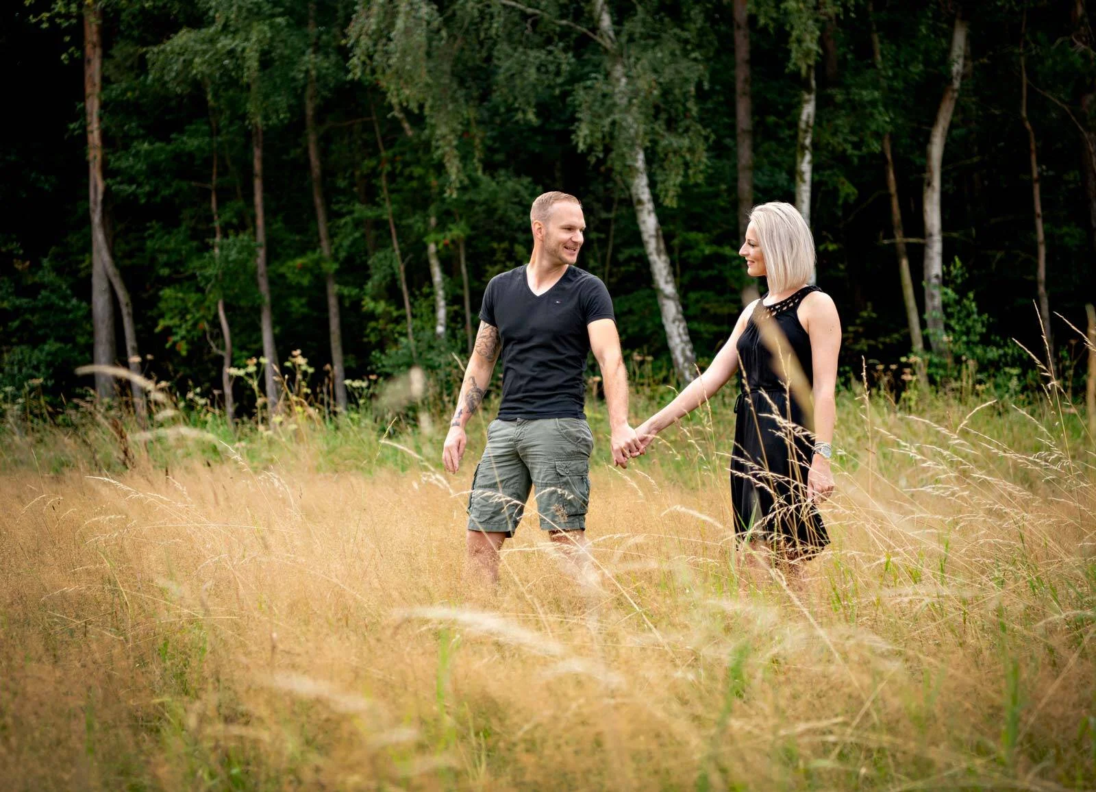 Pärchenfotoshooting: Paar geht Hand in Hand durch hohes, goldenes Gras vor Birken