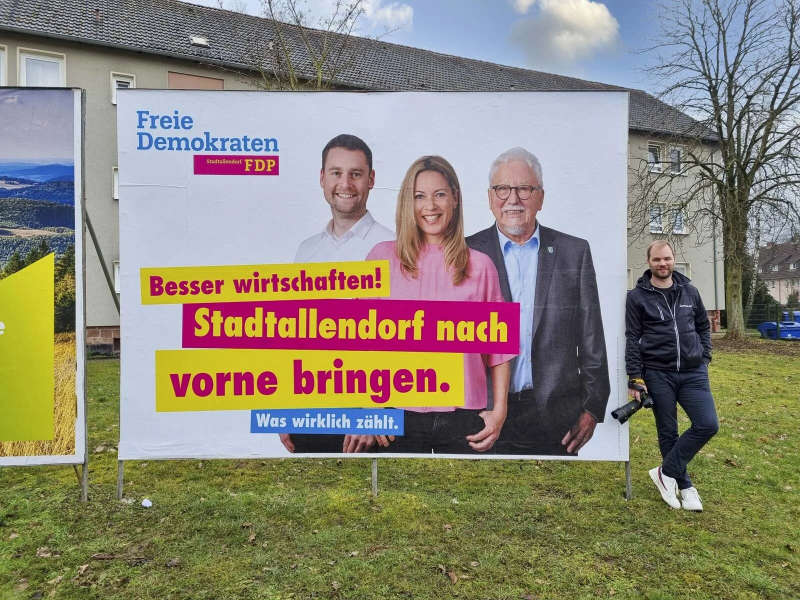 Wahlplakate zur Kommunalwahl: Fotograf neben einem Plakat mit drei Personen