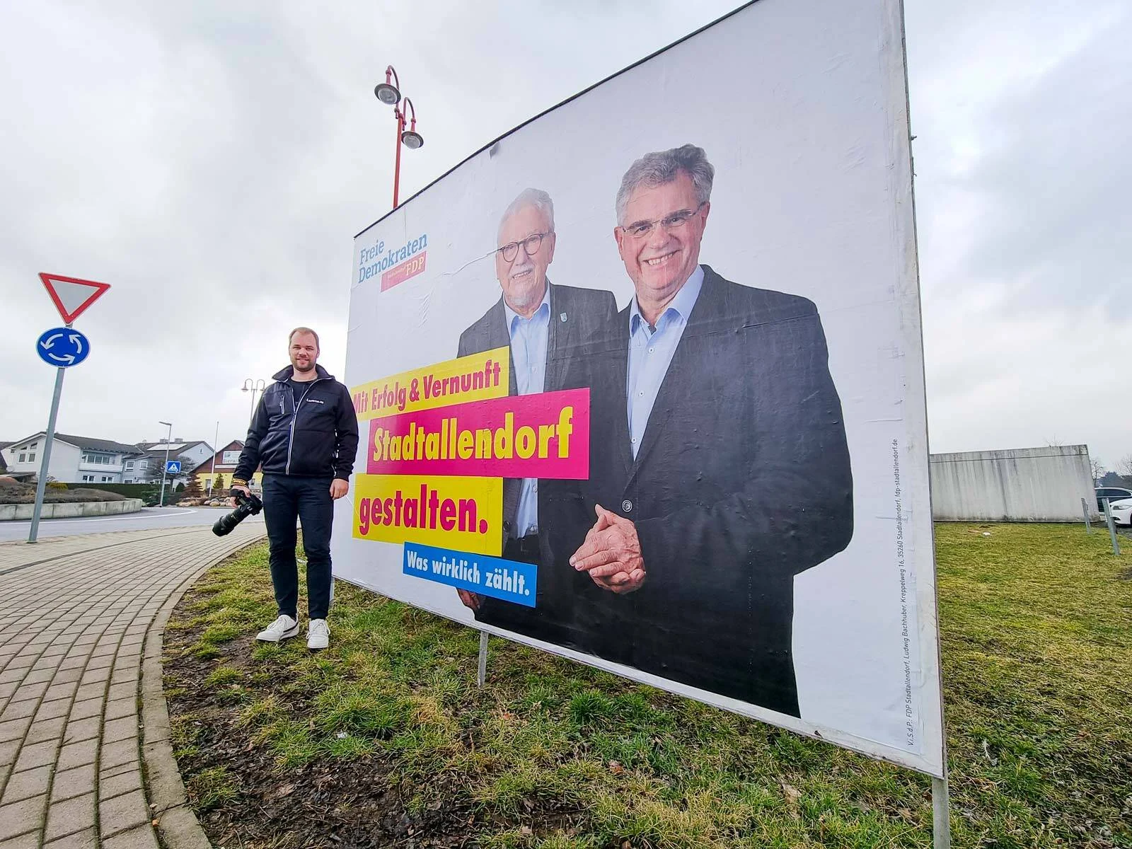 Wahlplakate in Stadtallendorf: Fotograf neben einem Plakat mit zwei Kandidaten an einem Kreisel