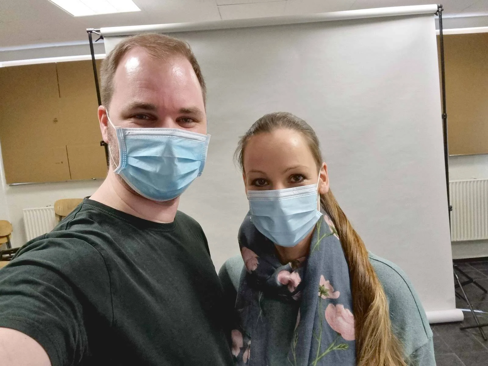 Zwei Personen mit Mund-Nasen-Schutz machen ein Selfie vor einem weißen Hintergrund