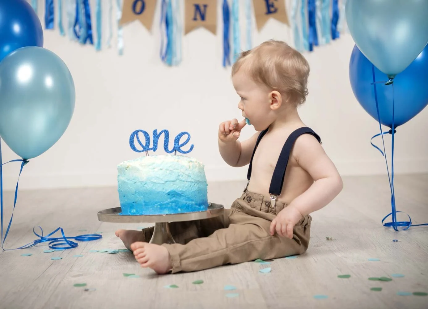 Kleiner Junge probiert vorsichtig Sahne von einer blauen Torte mit Schriftzug One