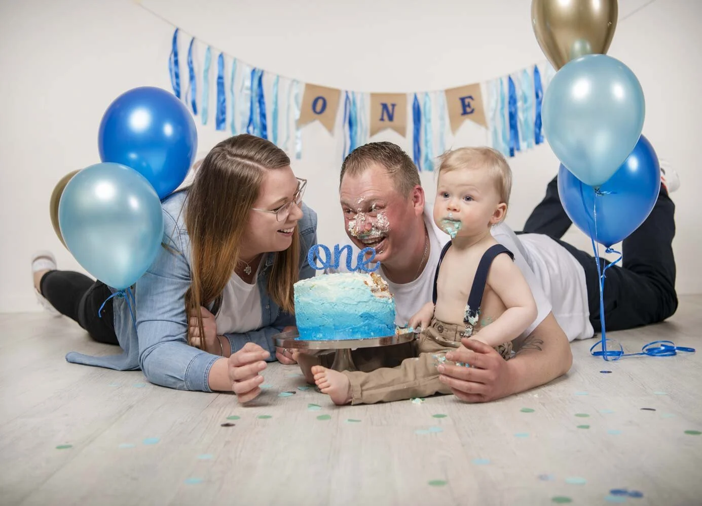 Familie liegt vor der Torte, Vater und Kind haben Sahne im Gesicht
