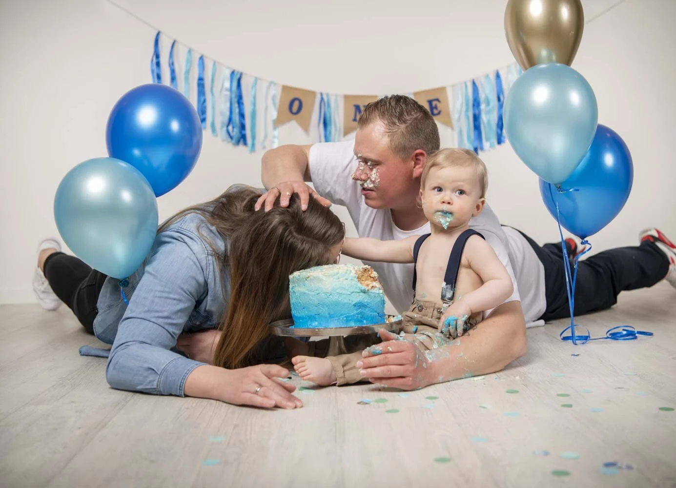 Cake Smash Fotoshooting: Mutter taucht das Gesicht in die Torte, der Vater lacht