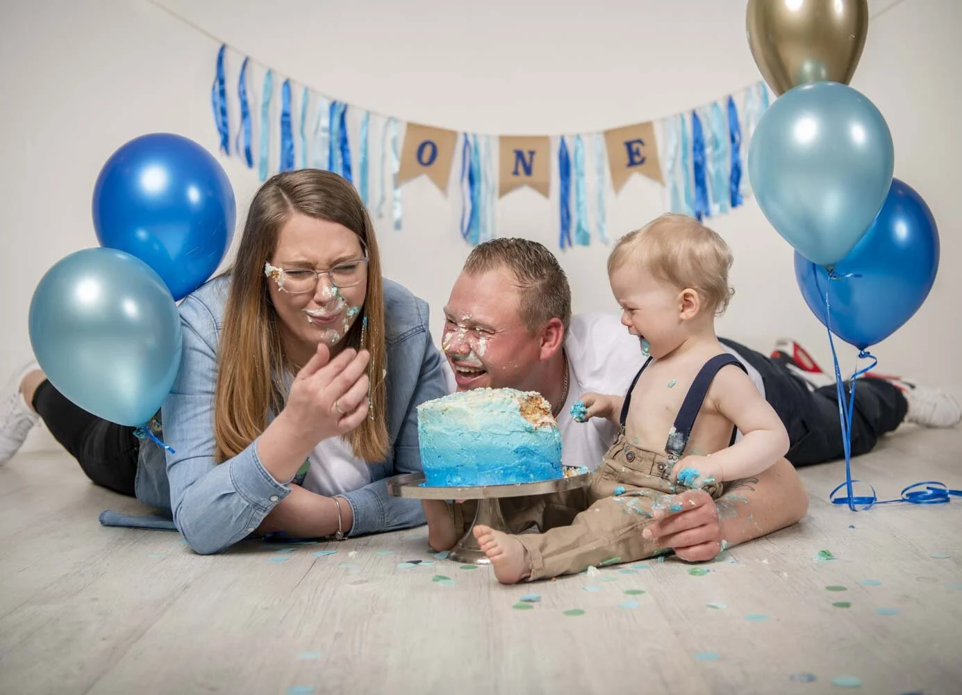 Eltern liegen auf dem Boden und probieren die Torte, das Kind schaut zu