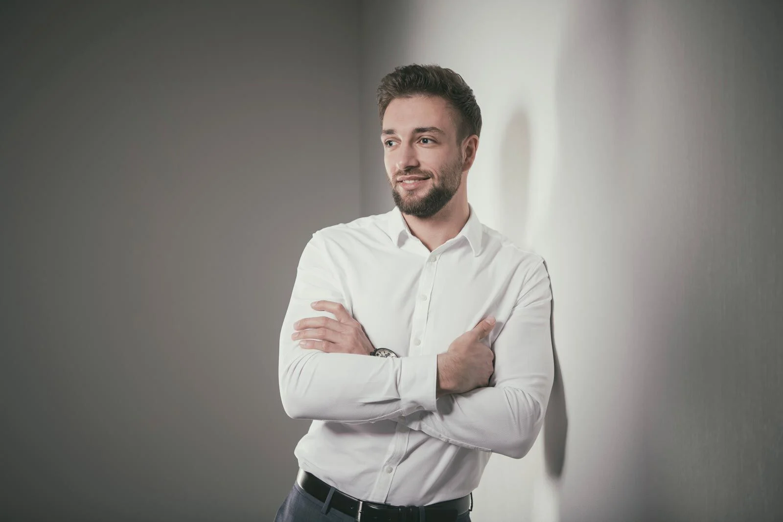 Männerportraits im Studio: Mann im weißen Hemd lehnt mit verschränkten Armen an einer Wand