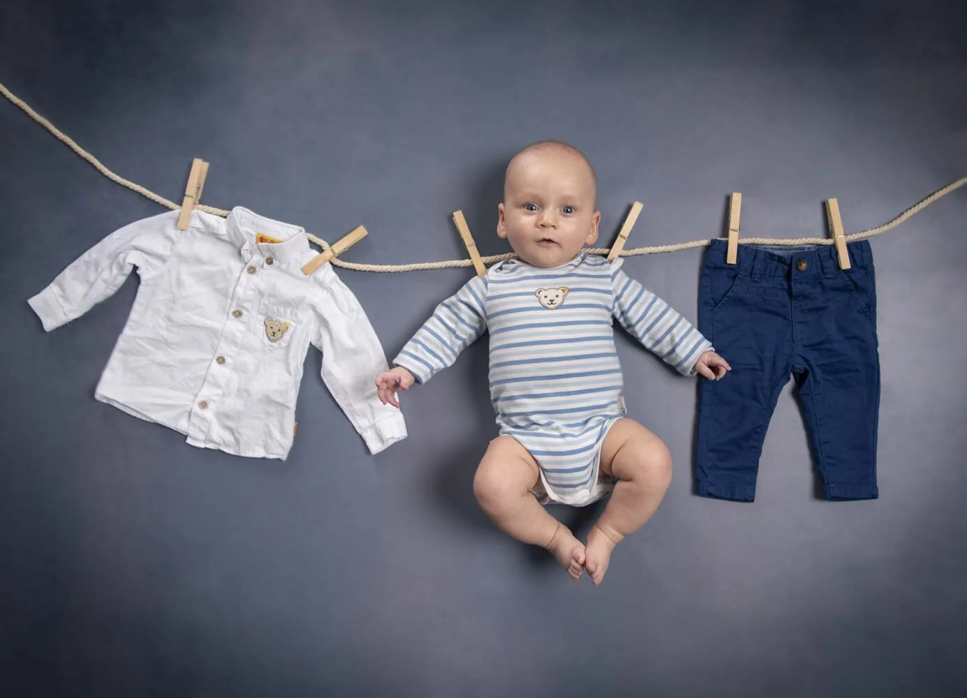 Baby im gestreiften Strampler zwischen Hemd und Hose an einer Wäscheleine