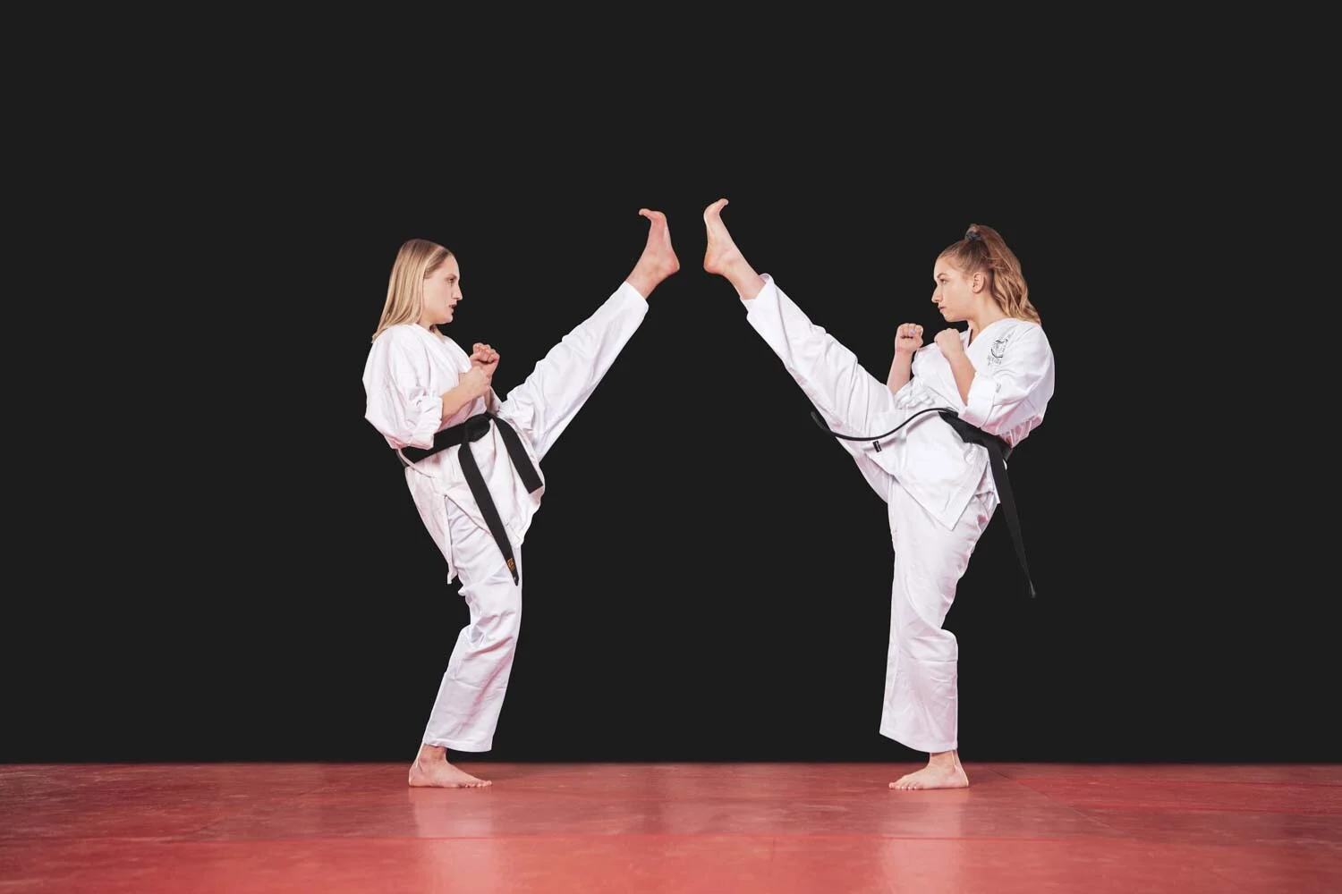 Zwei Karateka treten gleichzeitig mit gestrecktem Bein gegeneinander, dunkler Hintergrund