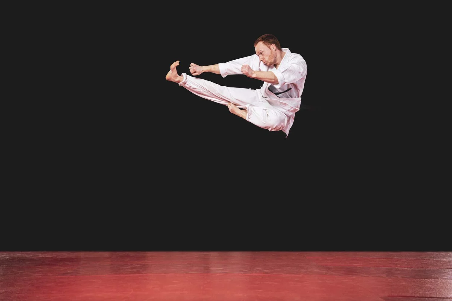 Karateka im weißen Anzug springt mit einem hohen Tritt über eine rote Matte