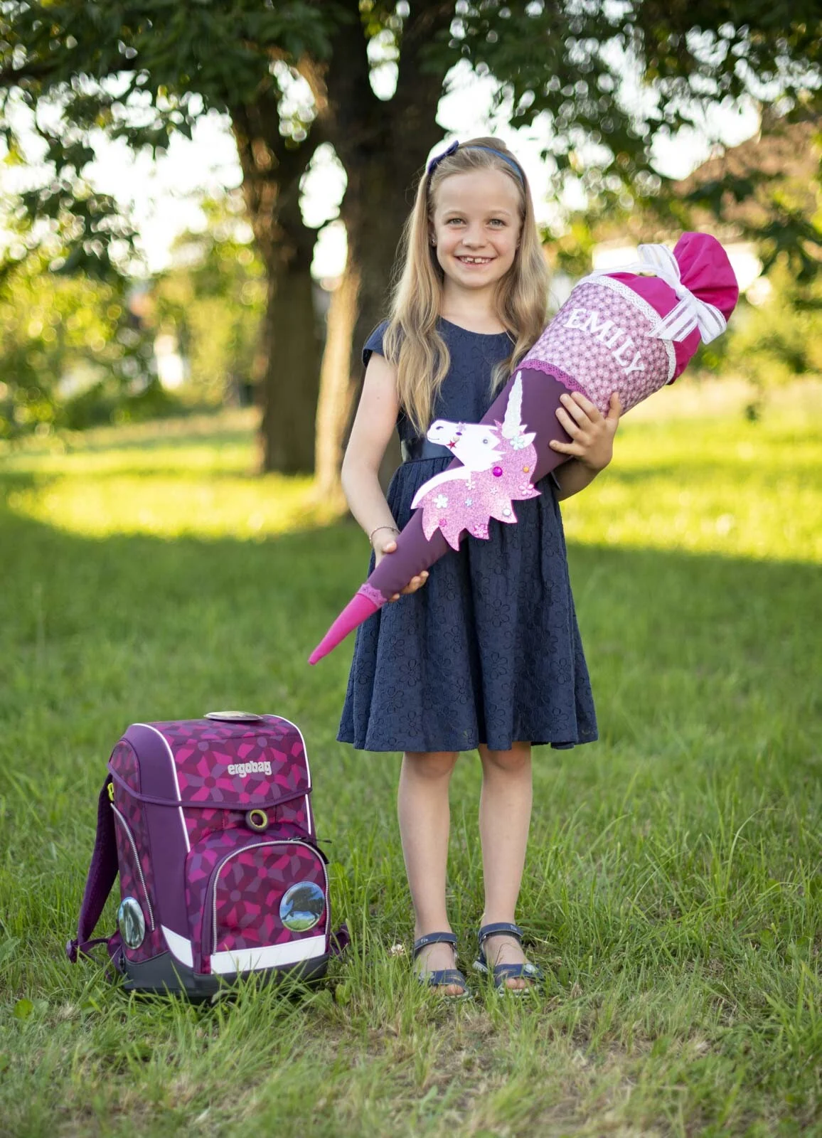 Mit Schulranzen | Peter Lauritis Photography Mädchen steht mit Schultüte auf der Wiese, daneben ihr lila Schulranzen