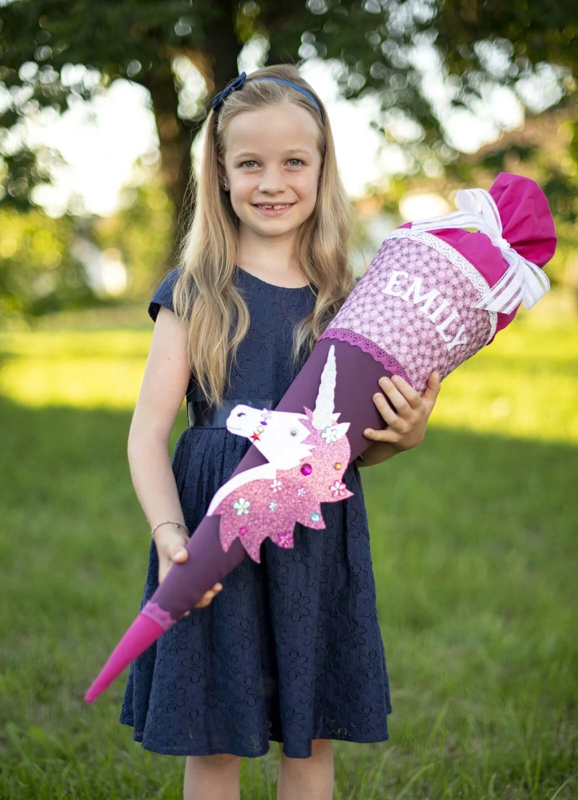 Einhorn-Schultüte | Peter Lauritis Photography Lachendes Mädchen im blauen Kleid hält eine lila Schultüte mit Einhorn