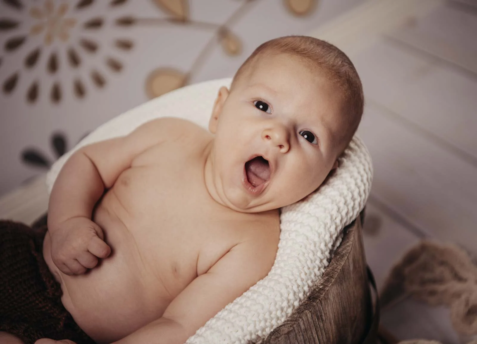Babyfotos: Baby gähnt herzhaft auf einer weißen Strickdecke in einer Holzschale