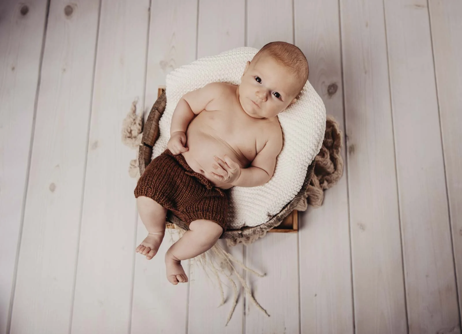 Baby auf weißem Kissen und Fell, von oben auf hellem Holzboden fotografiert