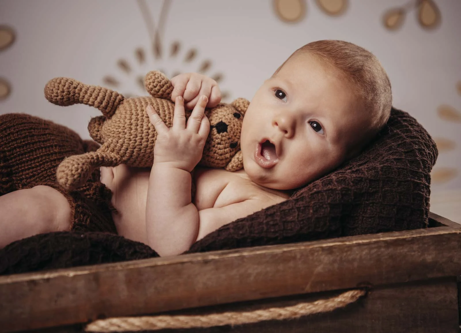 Babyfotos im Studio: Baby liegt auf brauner Strickdecke und hält einen gehäkelten Teddy