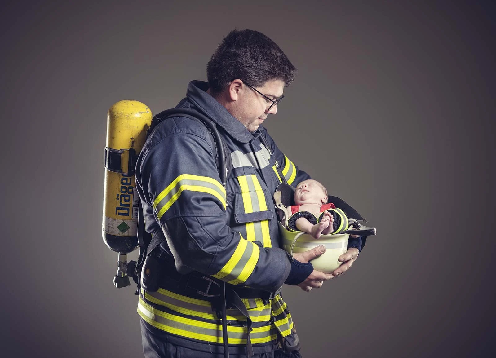 Vater mit Atemschutzgerät auf dem Rücken hält das Baby in einem weißen Helm