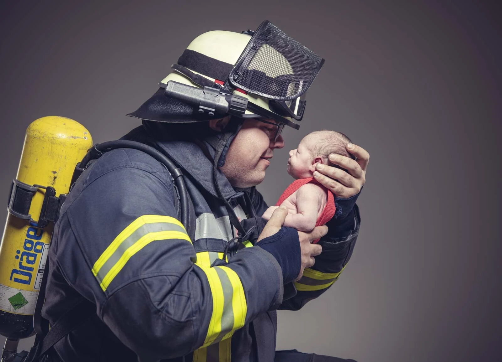 Feuerwehrmann mit Helm und Visier hält sein Neugeborenes Nase an Nase vor sich