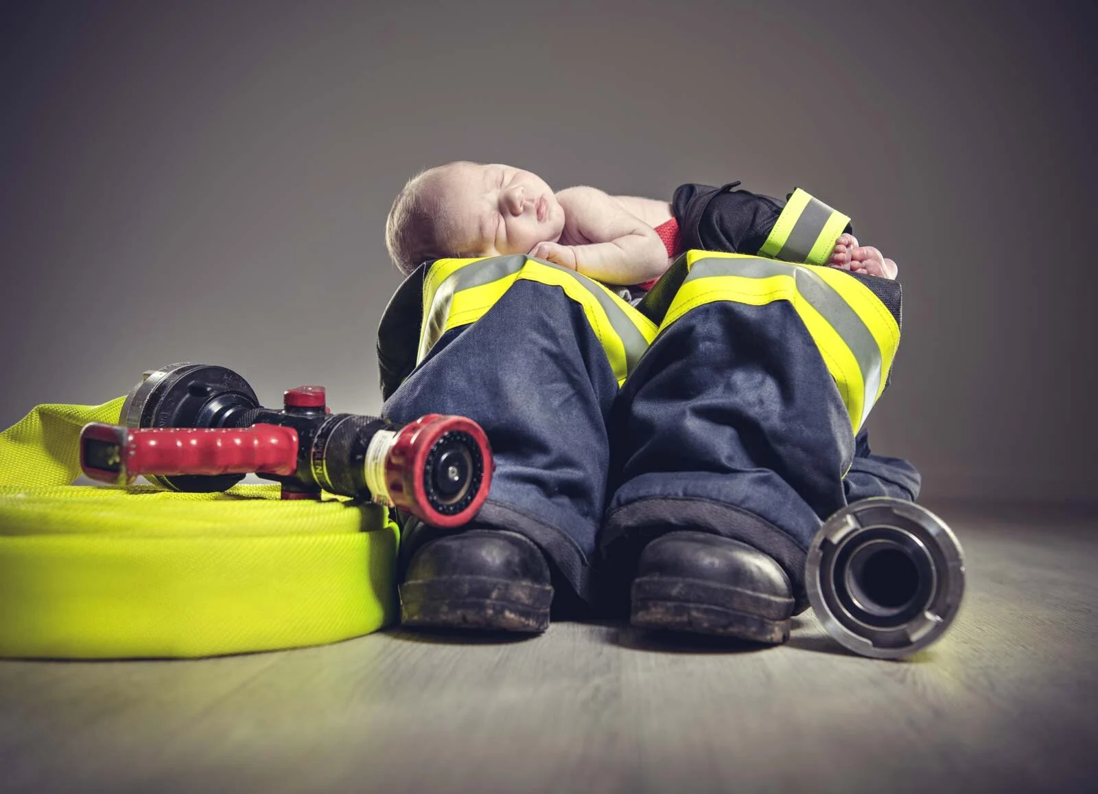 Babyfeuerwehrmann schläft auf einer Einsatzhose neben Stiefeln, Schlauch und Strahlrohr