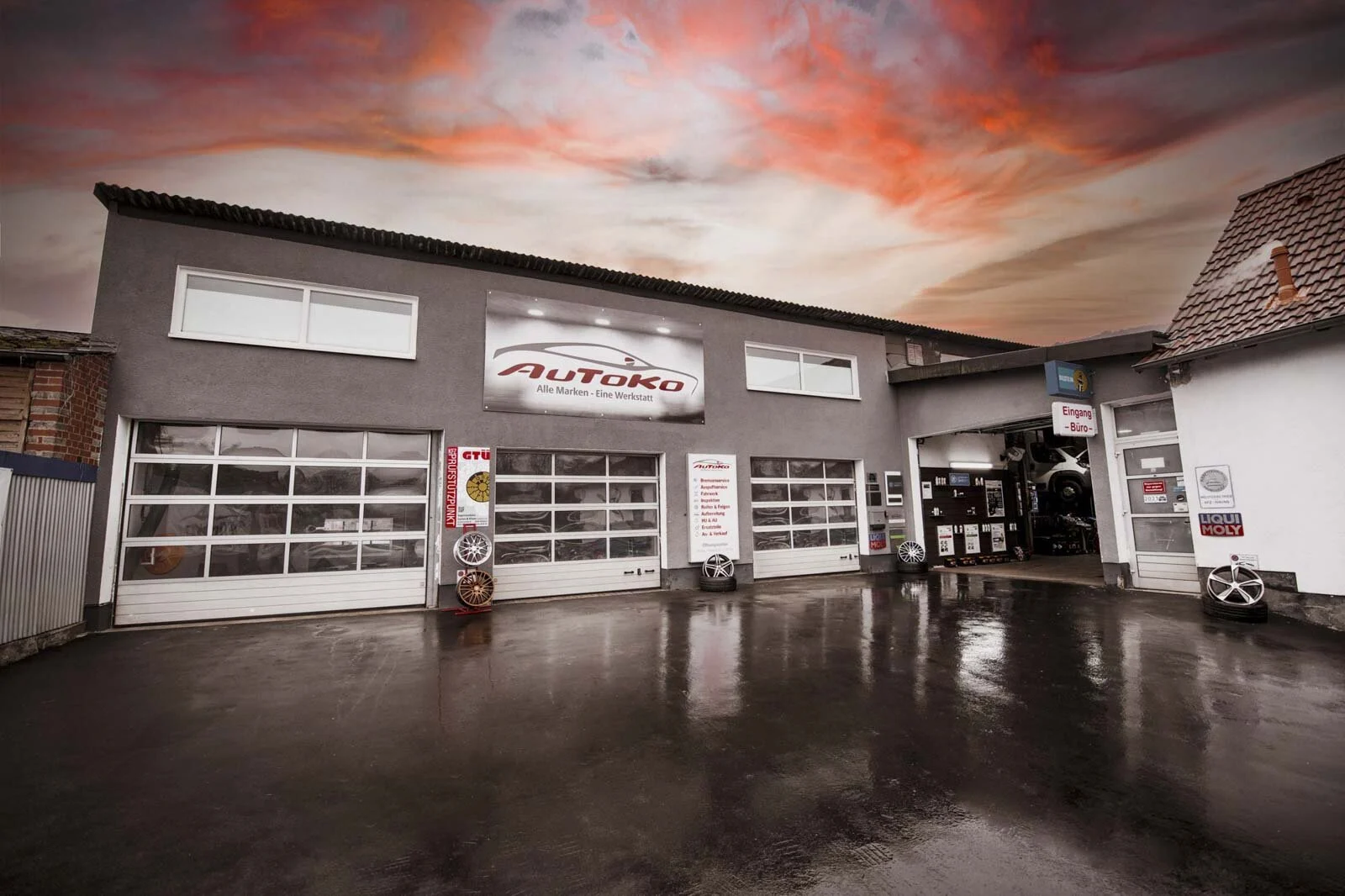 Gebäude der Autowerkstatt mit Rolltoren und Logo unter einem rötlichen Abendhimmel