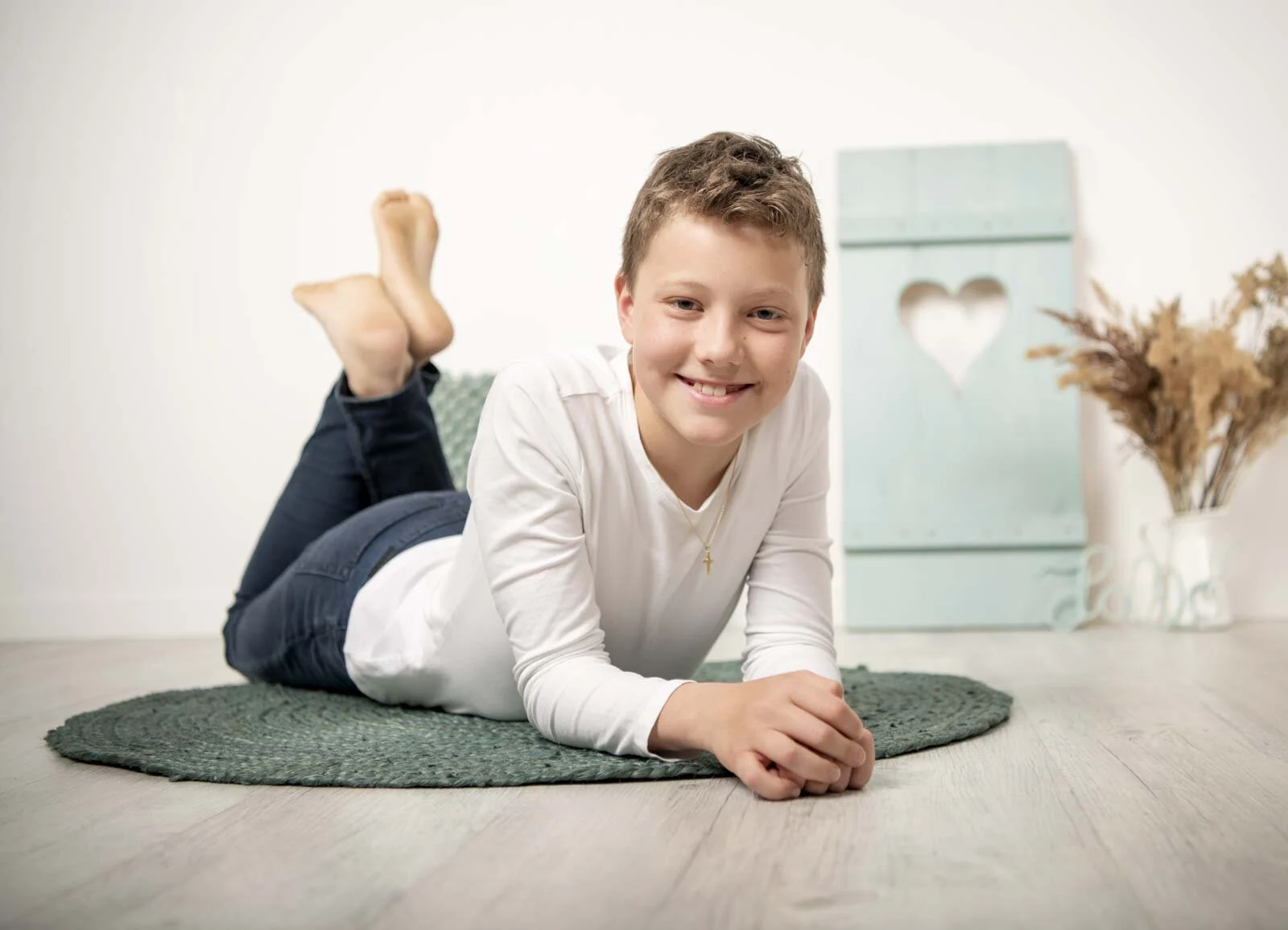 Kinderfotograf im Studio: Junge liegt lachend auf einem grünen Teppich, die Füße in der Luft