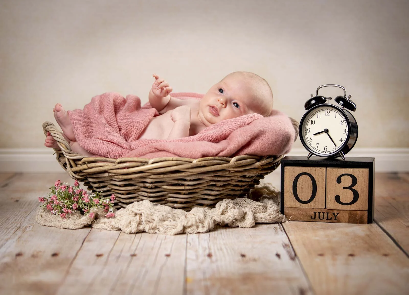 Baby liegt im Weidenkorb, daneben ein Wecker und Holzwürfel mit Datum