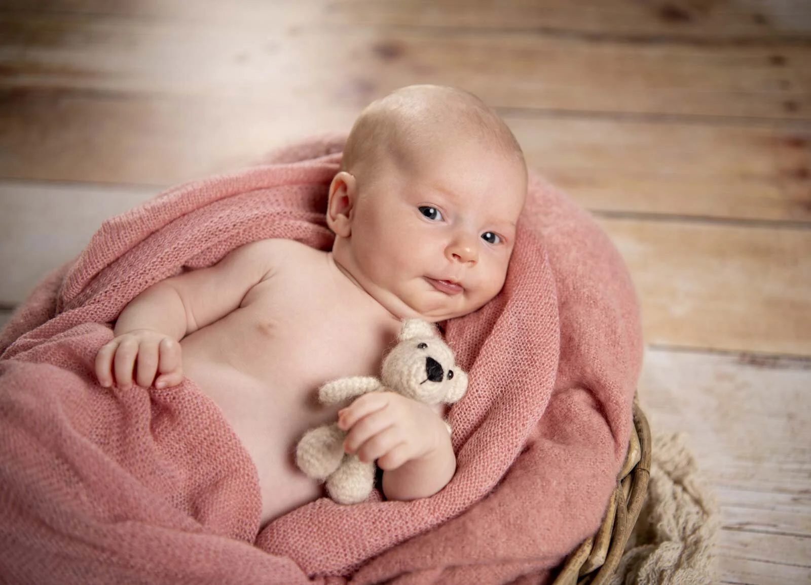Baby mit großen Augen hält einen kleinen weißen Teddy, eingewickelt in ein rosa Tuch