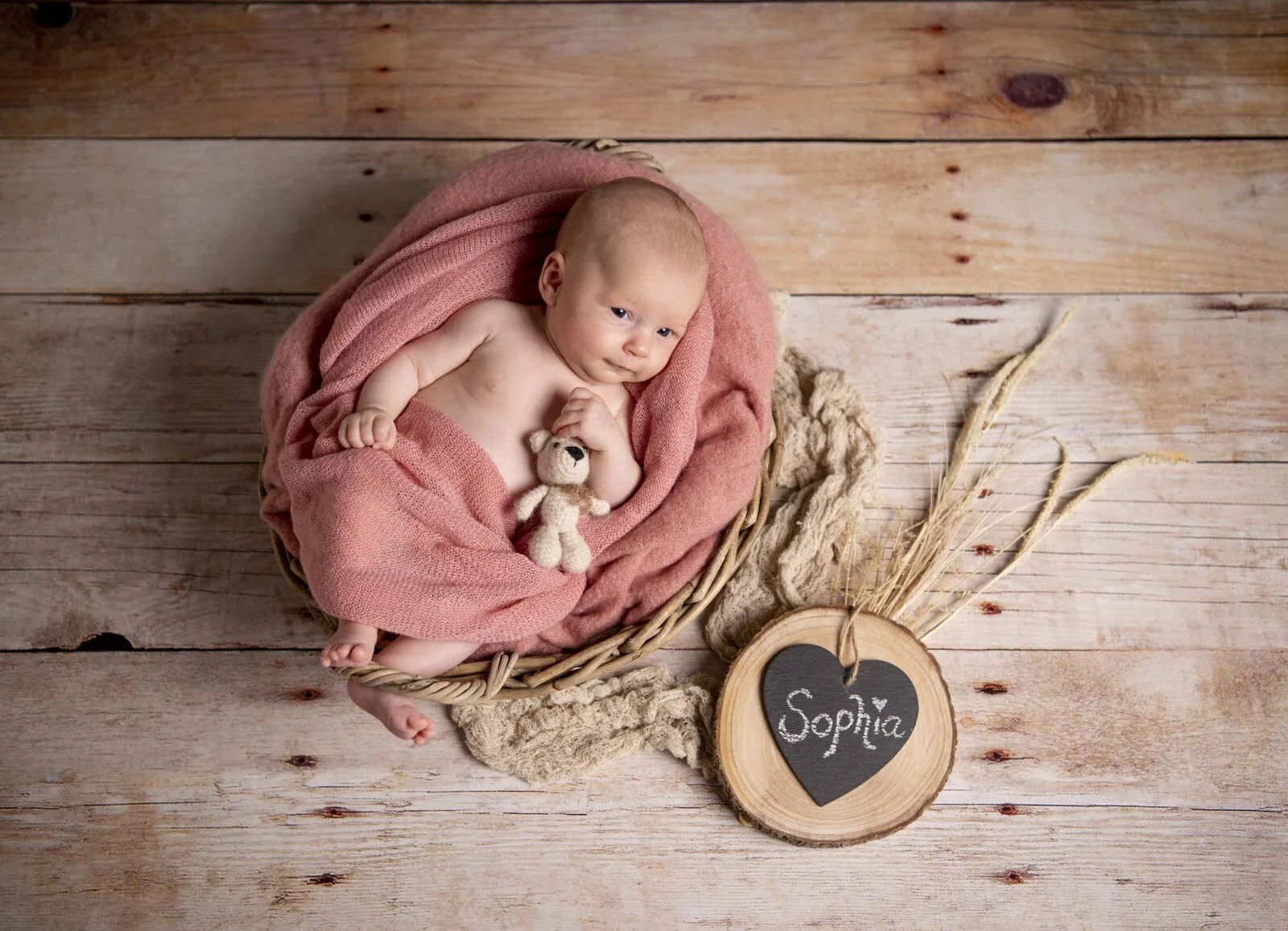 Babypass Newborn-Shooting: Baby im rosa Tuch in einem Körbchen auf hellem Holzboden