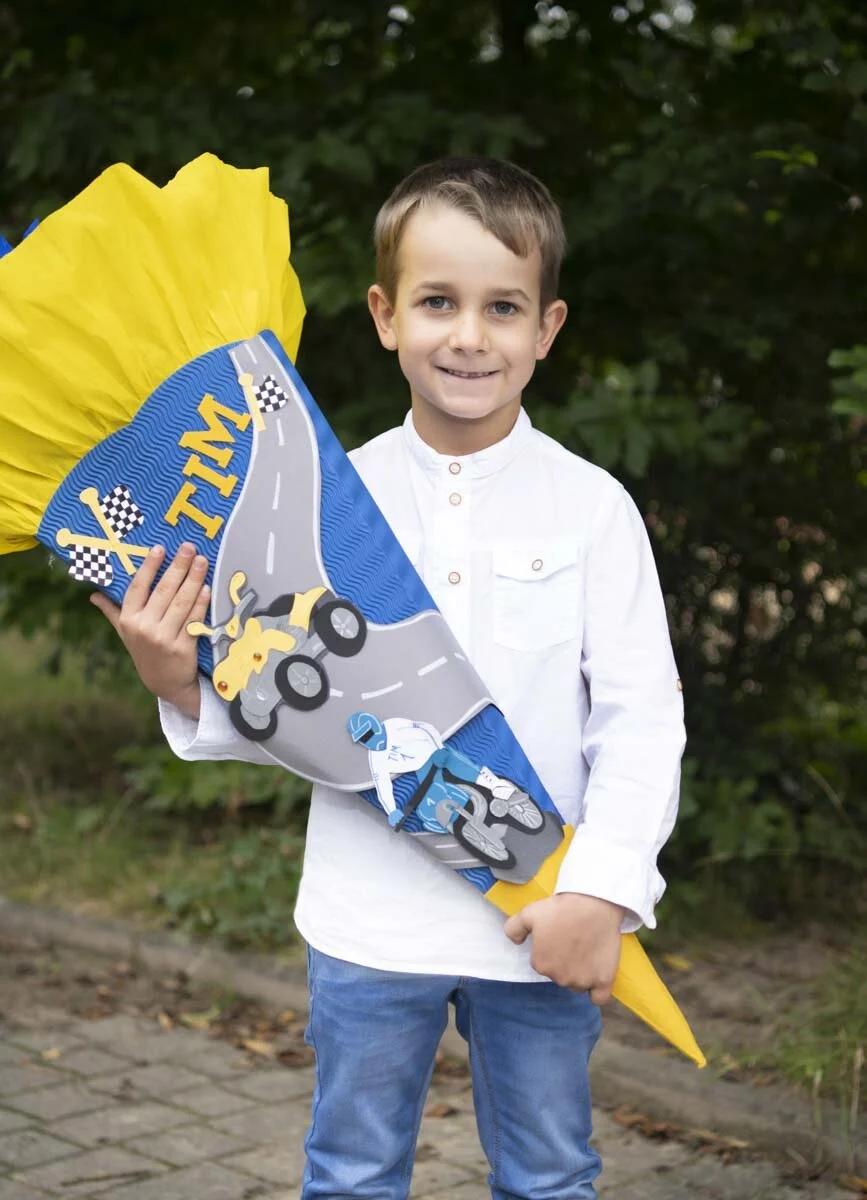 Junge im weißen Hemd hält eine blau-gelbe Schultüte mit Rennwagen