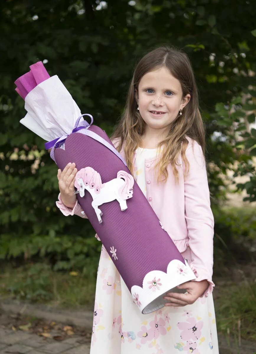 Mädchen im rosa Kleid hält eine lila Schultüte mit Einhorn