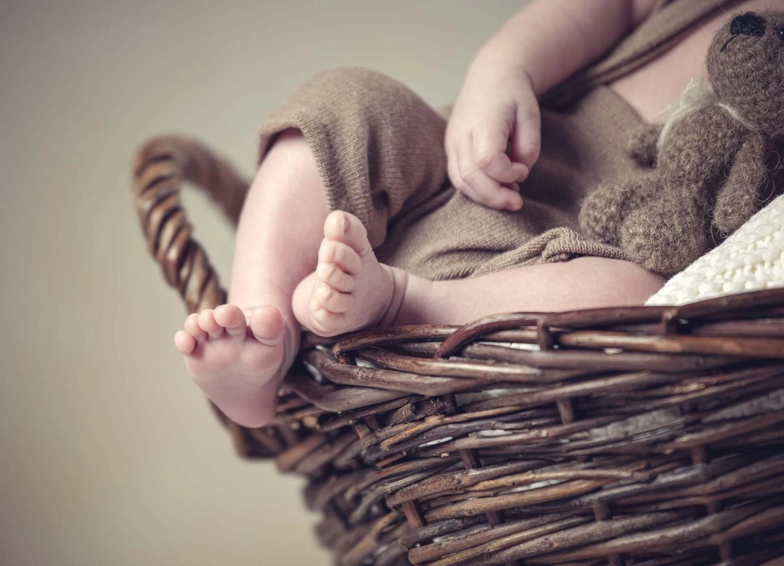 Winzige Babyfüße am Rand eines Weidenkorbs, daneben ein Teddy aus Strick
