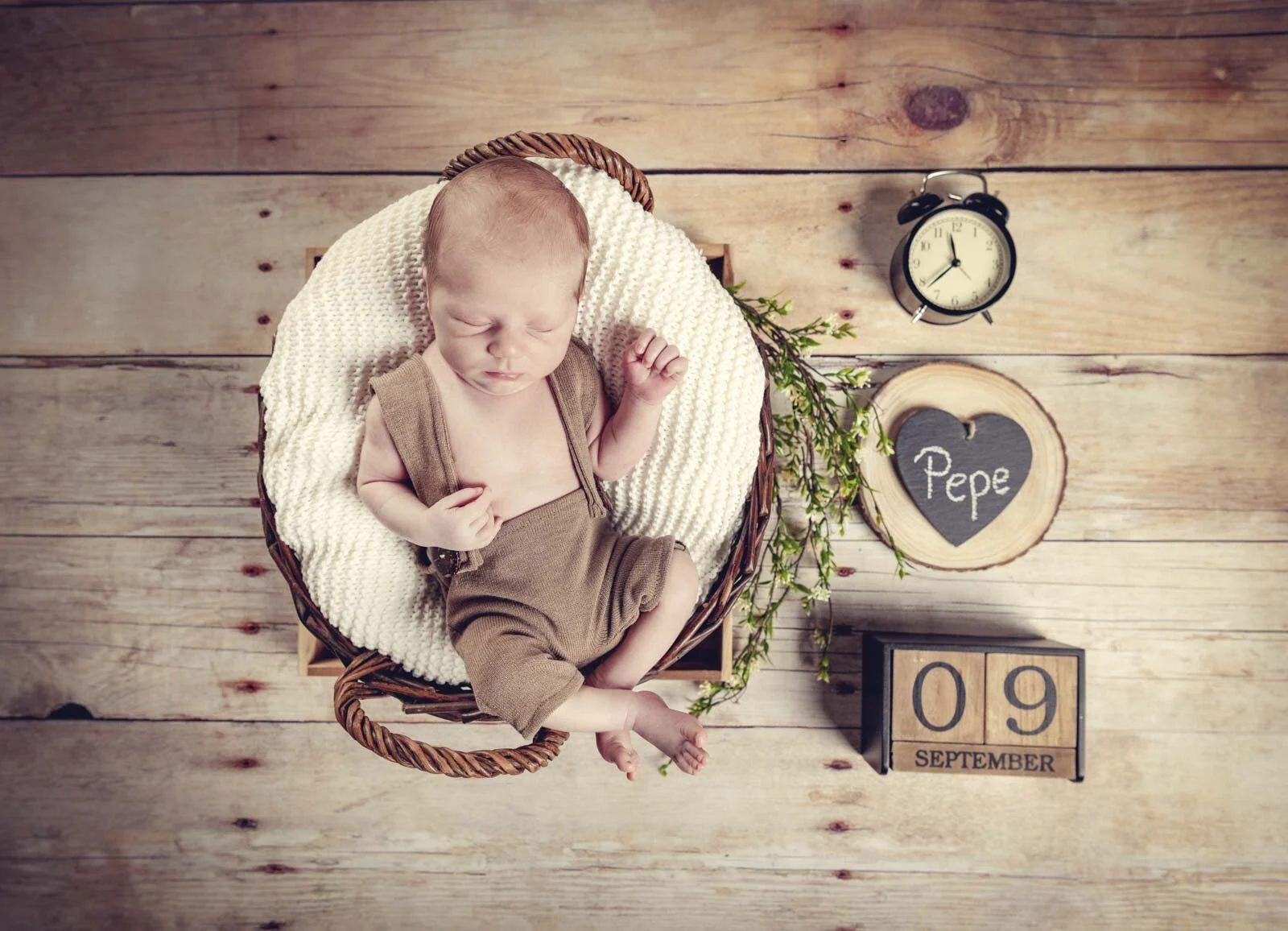 Newborn Fotoshooting von oben: Baby im Korb auf Holzboden, daneben Wecker und Datumswürfel