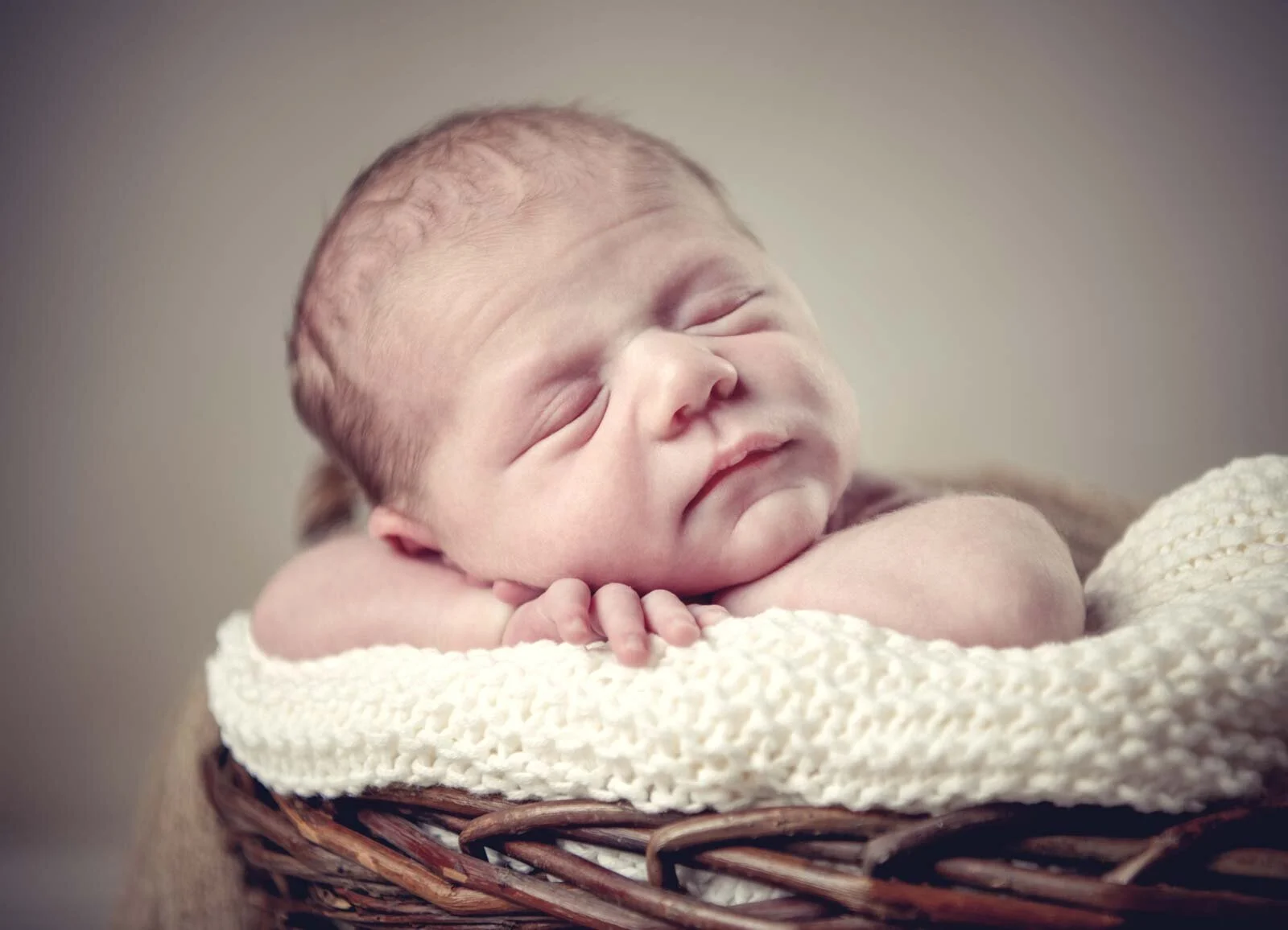 Nahaufnahme eines schlafenden Babys mit den Händen unter dem Kinn auf einem Weidenkorb
