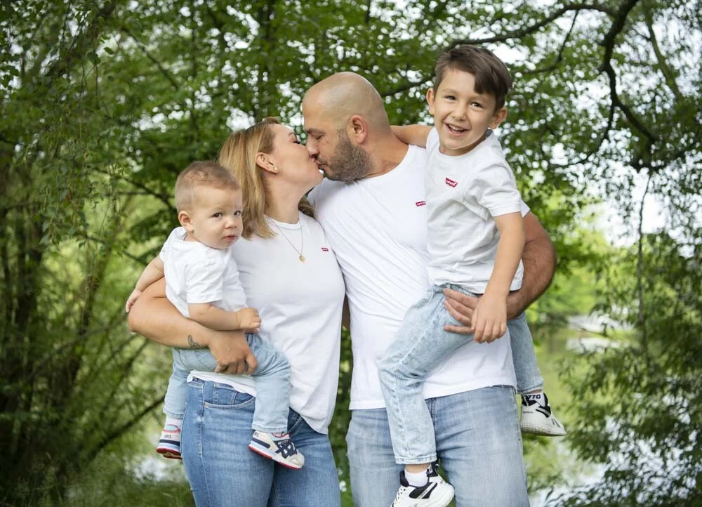 Eltern küssen sich, Vater hält den älteren Sohn, Mutter das Kleinkind auf dem Arm