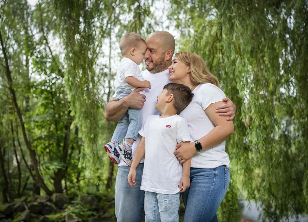 Outdoor Familienfotoshooting: lachende Familie in enger Umarmung vor grünen Weidenzweigen