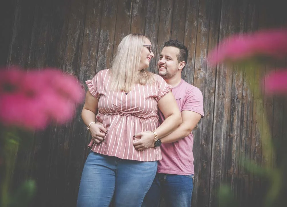 Vor der Holzwand | Peter Lauritis Photography Pärchen Fotoshooting vor einer alten Holzwand, vorn unscharfe pinke Blüten