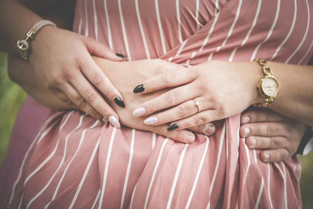 Nahaufnahme verschränkter Hände mit Ring, goldener Uhr und Armband auf gestreiftem Kleid