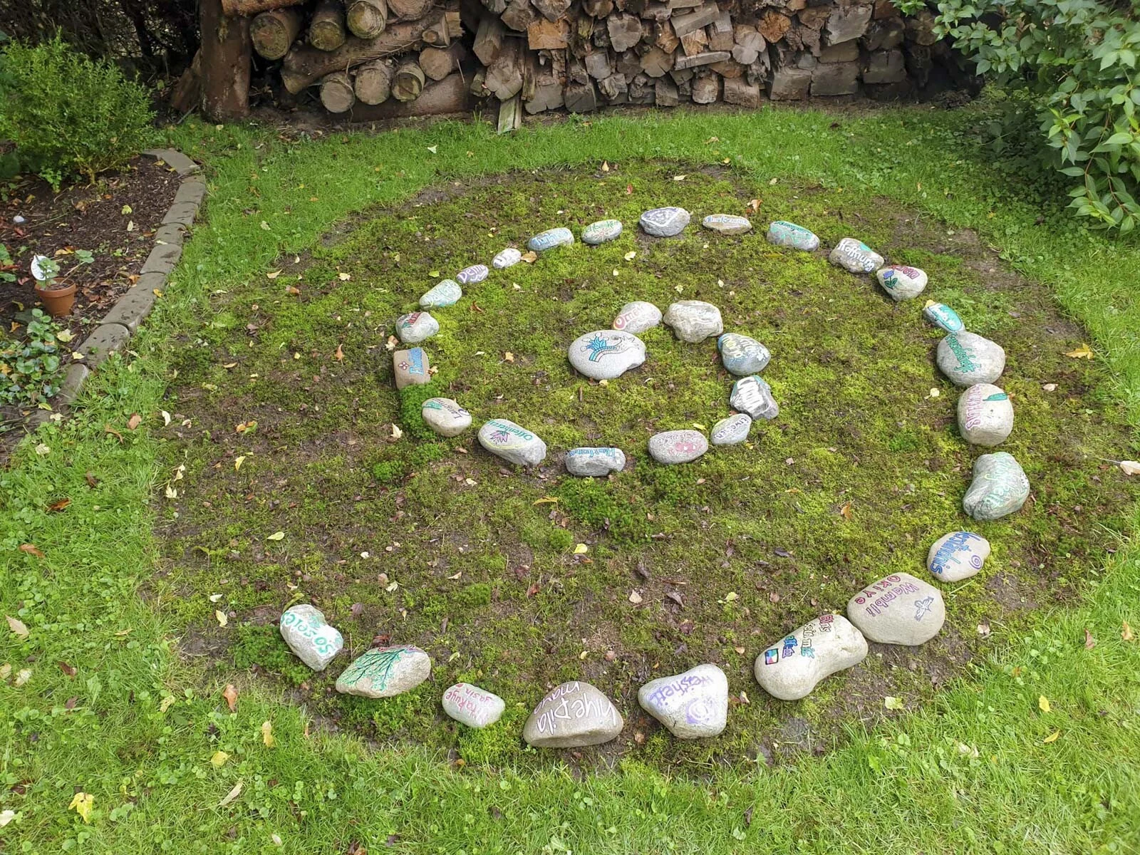 Atlachinolli Energiespirale aus hellen Steinen auf einer Wiese vor einem Holzstapel