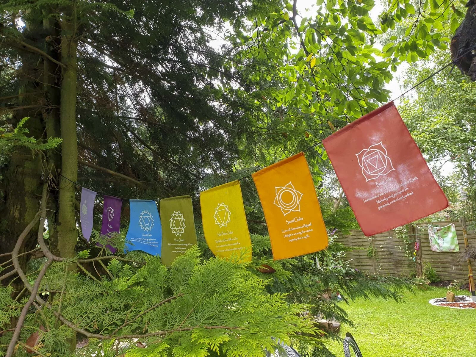 Bunte Stofffahnen mit Symbolen hängen an einer Leine zwischen Bäumen im Garten