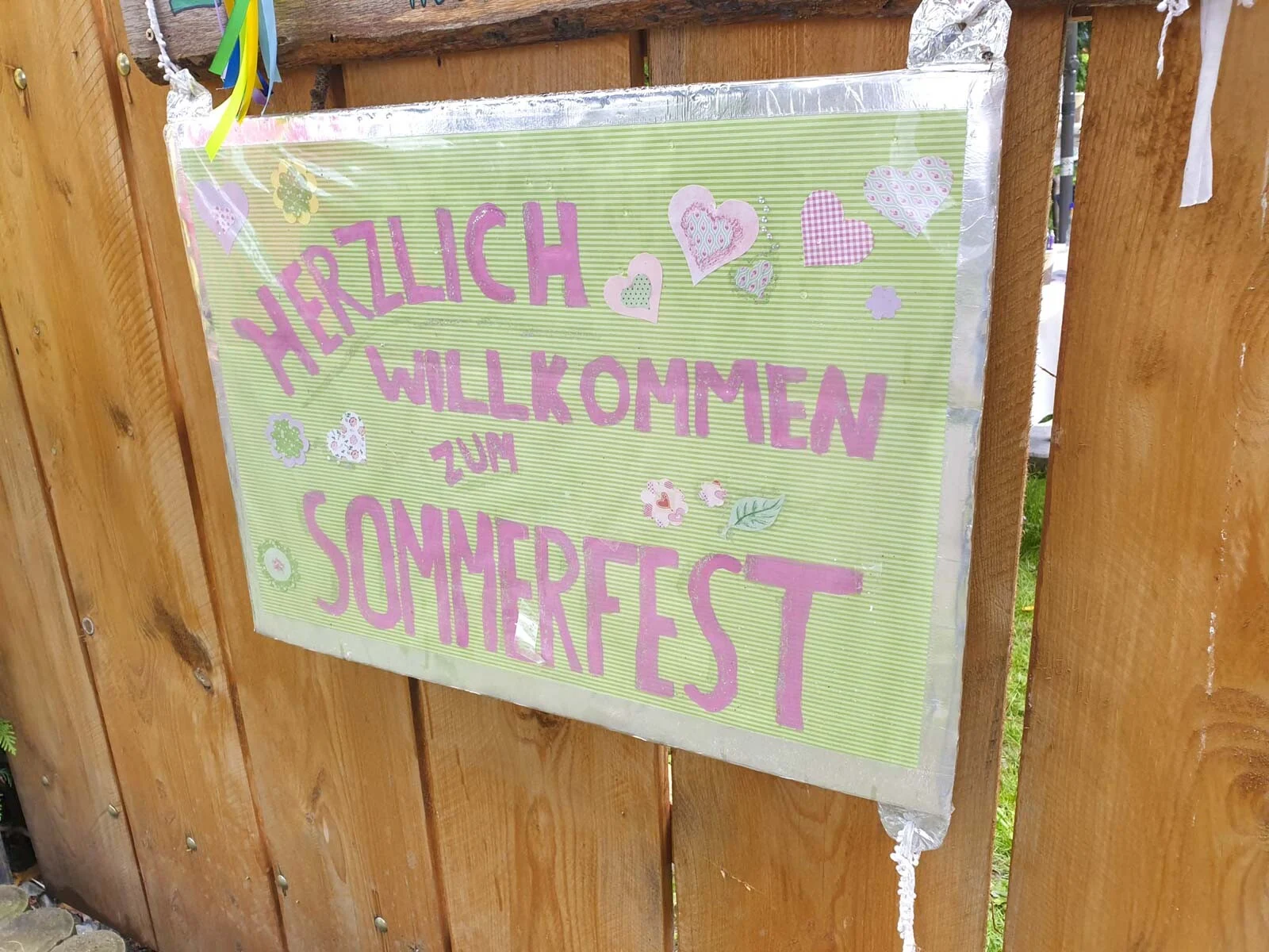 Buntes Schild mit Herzlich willkommen zum Sommerfest an einem Holztor