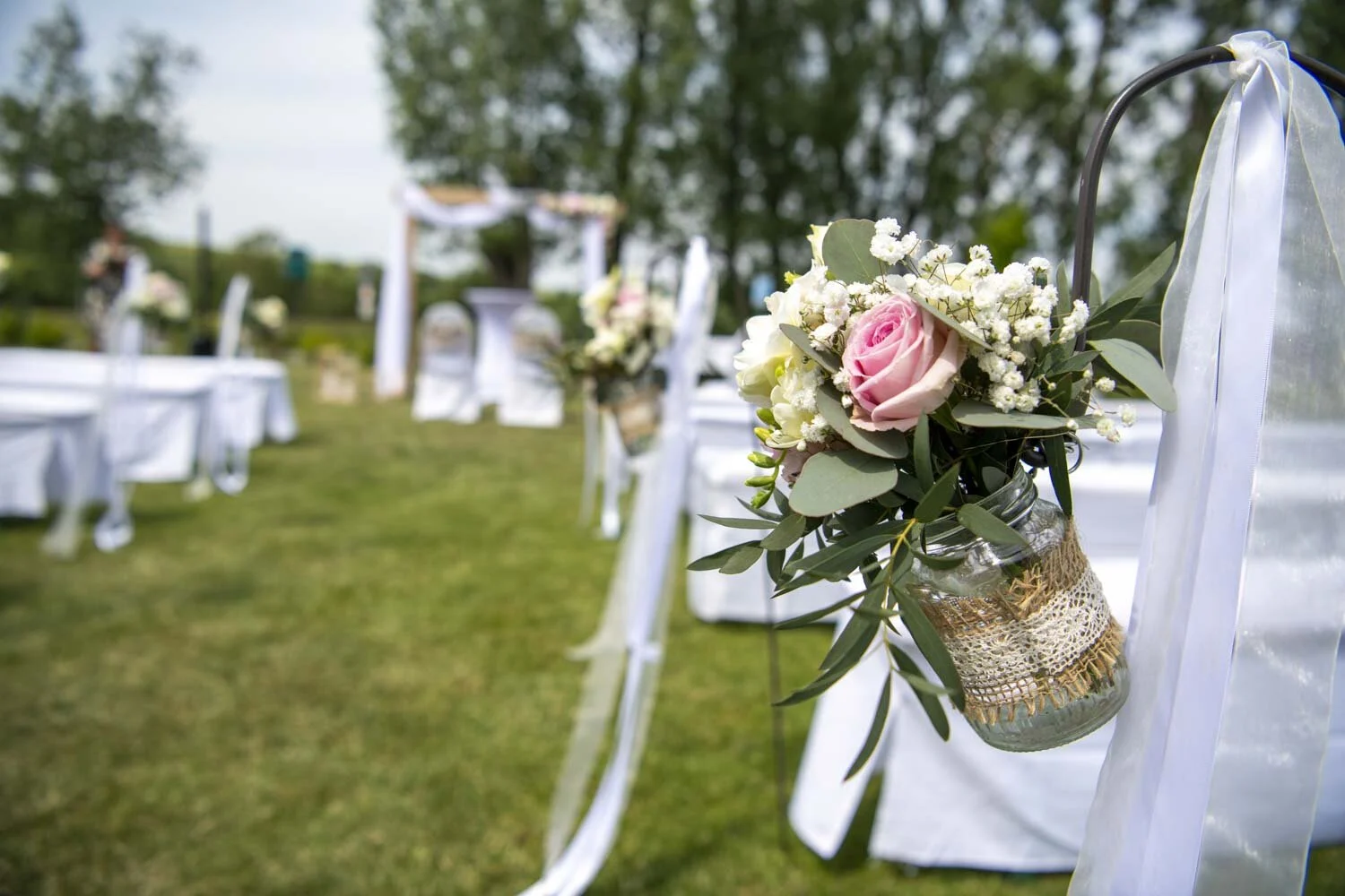 Kleines Glas mit rosa Rosen und Schleierkraut an einem Haken am Mittelgang