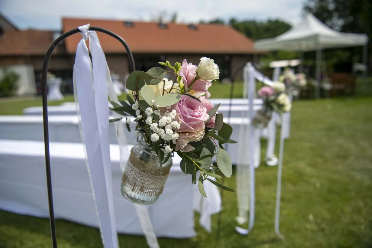 Glas mit Rosen an einem weißen Band, im Hintergrund ein Pavillon